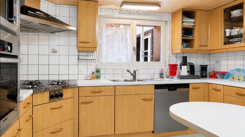 A modern kitchen with wooden cabinets, stainless steel appliances, and a central island. The space includes a stove, oven, sink, dishwasher, coffee maker, and various kitchen items on the counter.
