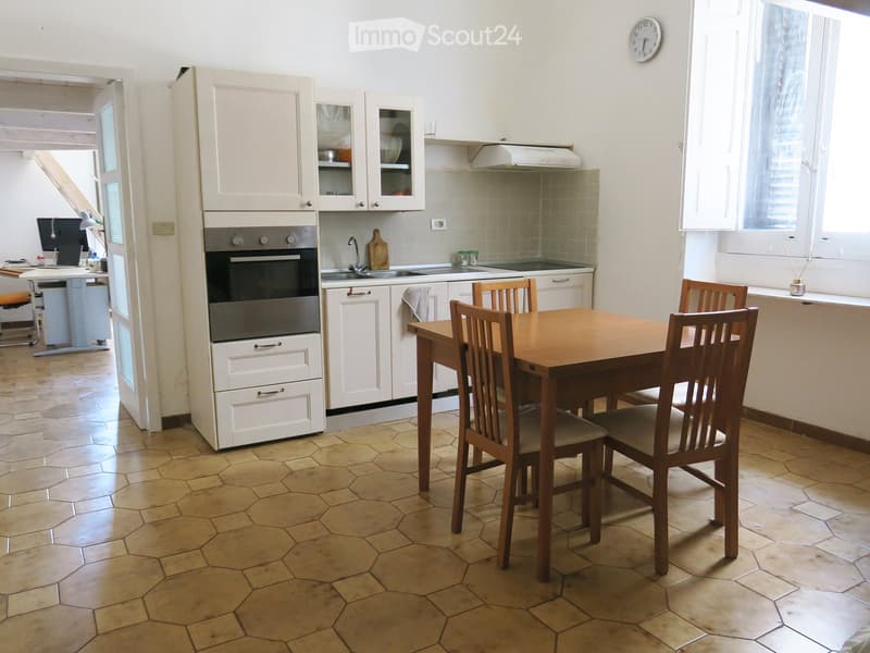 Bright kitchen with white cabinets, a wooden dining table with chairs, an oven, sink, and a window with blinds.