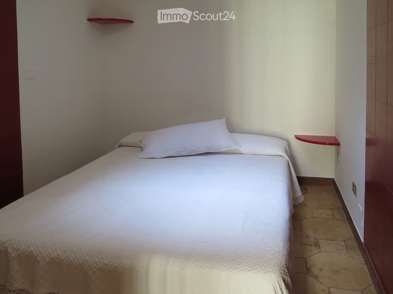 Small bedroom with a single bed, white bedding, and two red wall shelves.