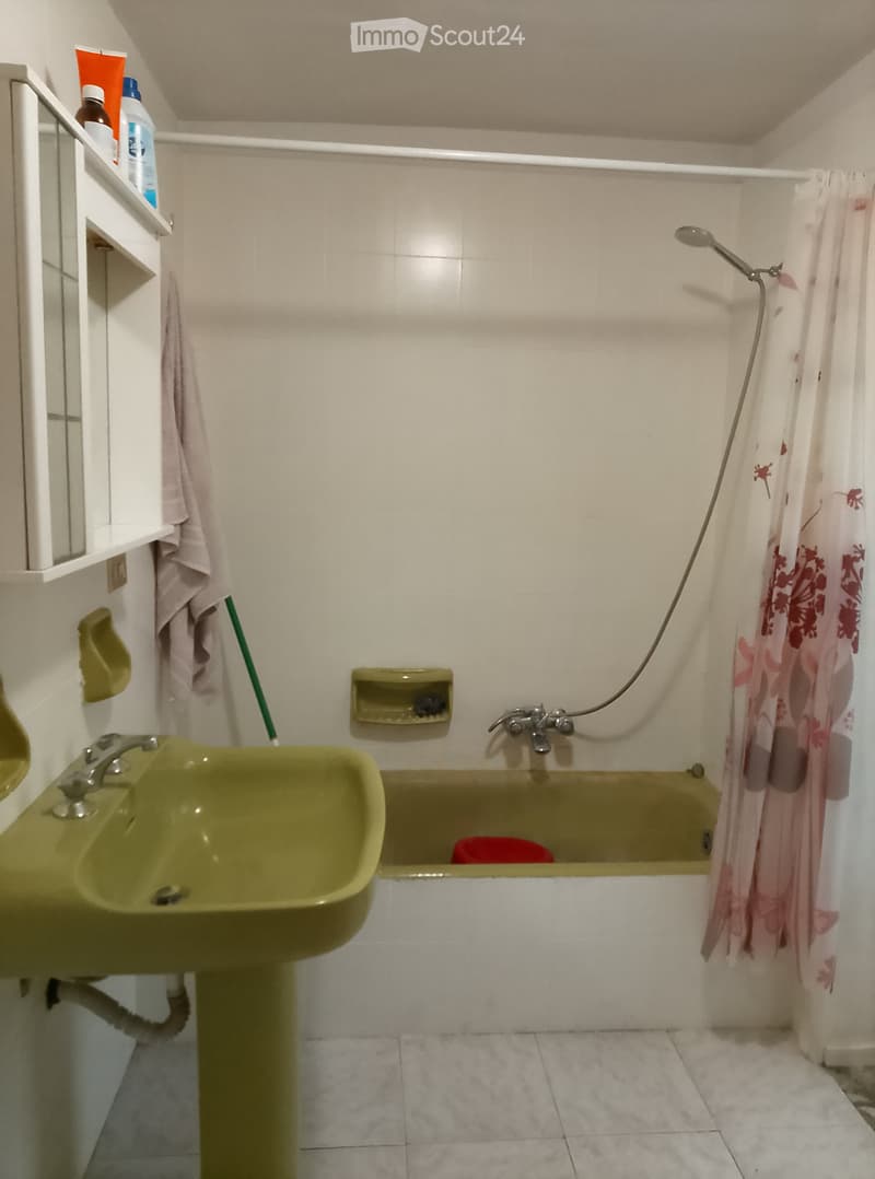 Bathroom with green sink, bathtub, shower curtain, towel, and shelf with bottles.