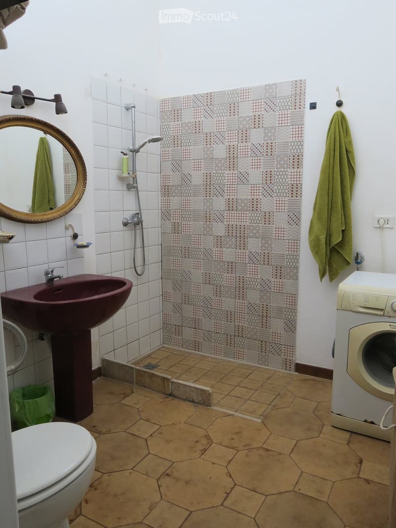 Bathroom with hexagonal tile floor, white tiled walls, a dark red sink, a toilet, a shower area with patterned tiles, a mirror, and a washing machine.