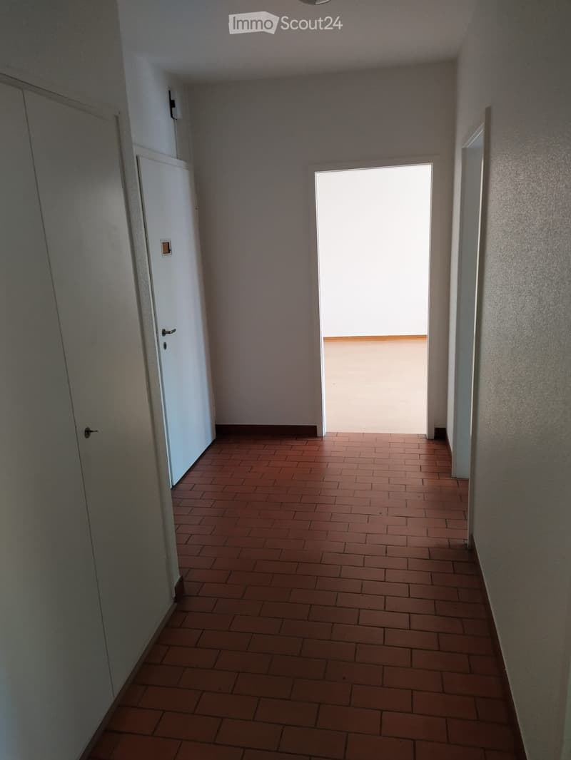 Empty hallway with tiled floor, white walls, and a door leading to a bright area.