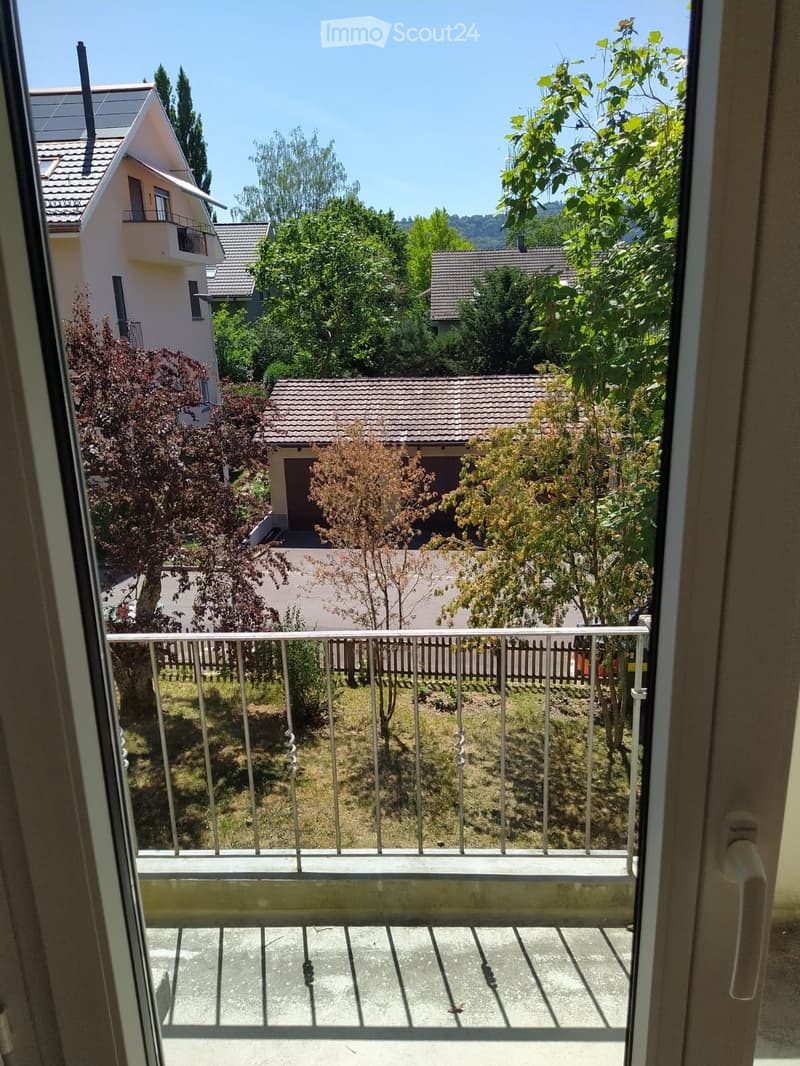 Balcony with metal railing overlooking a residential area with houses, trees, and a clear blue sky.