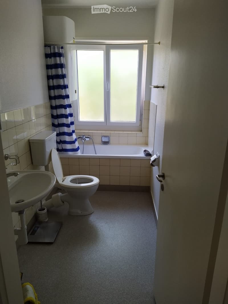 Bathroom with a toilet, sink, bathtub, and window with a blue and white striped curtain.