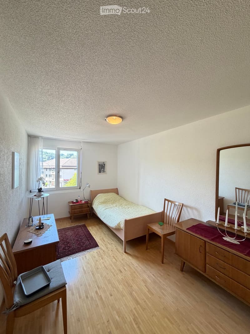 Cozy bedroom with wooden floor, bed, desk, chair, mirror, and side table.