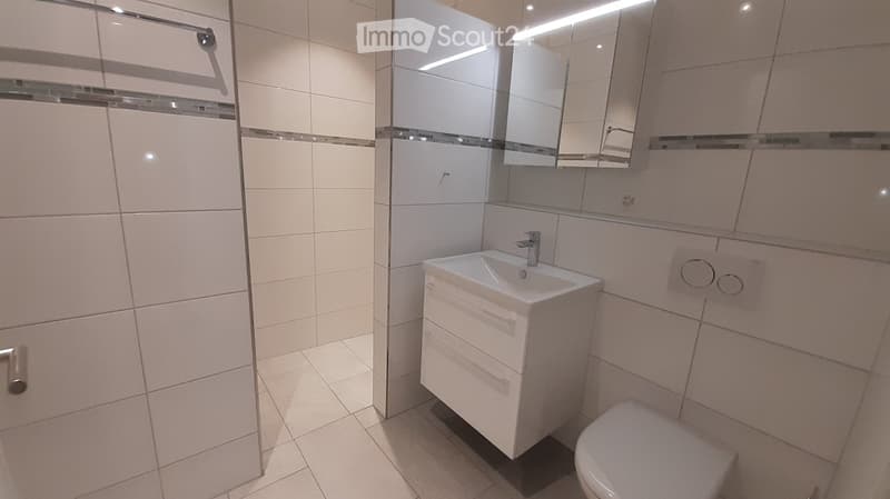 Modern bathroom with white tiles, a white sink with a mirror cabinet, and a toilet.