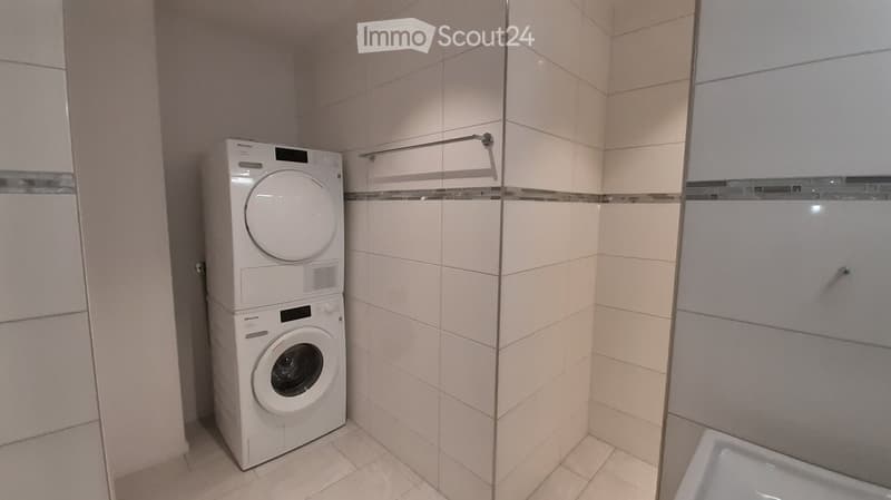 Bathroom with a stacked washing machine and dryer unit, tiled walls, and a towel rack.