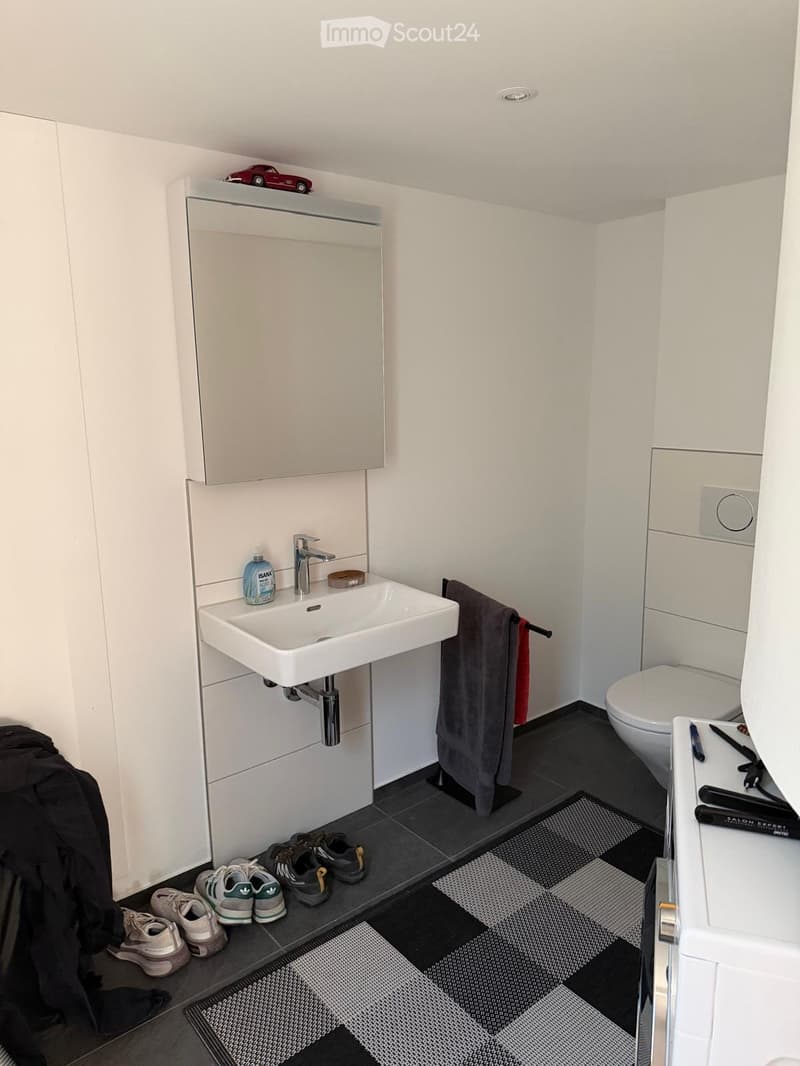 Modern bathroom with white walls, dark tiled floor, sink, faucet, toilet, towel, cabinet, and a small car toy on top of the cabinet.