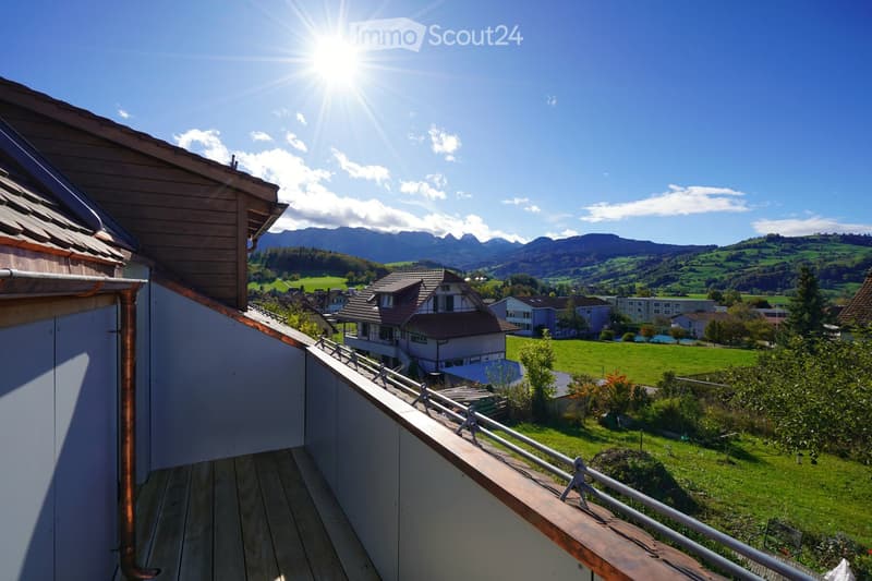 Balcony overlooking a green landscape with houses and mountains in the background.