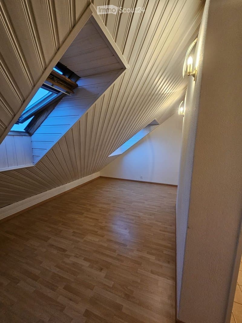 An empty attic space with wooden flooring, slanted wooden ceiling, and skylight windows allowing natural light to enter.