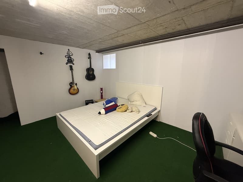 A small bedroom with a single bed, pillows, a guitar on the wall, a chair, and a toy on the bed.