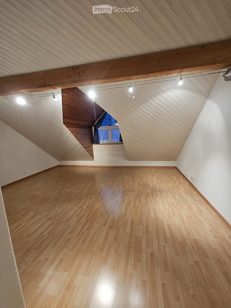 Empty attic room with wooden flooring, exposed wooden beams, and a skylight window. No furniture or equipment present.