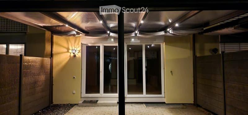 Covered outdoor area with a raised ground floor, featuring a glass door entrance, yellow walls, and modern lighting fixtures.