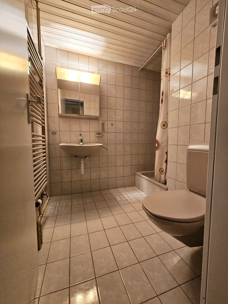 Modern bathroom with tiled walls and floor, featuring a sink, mirror, toilet, bathtub, and shower curtain.