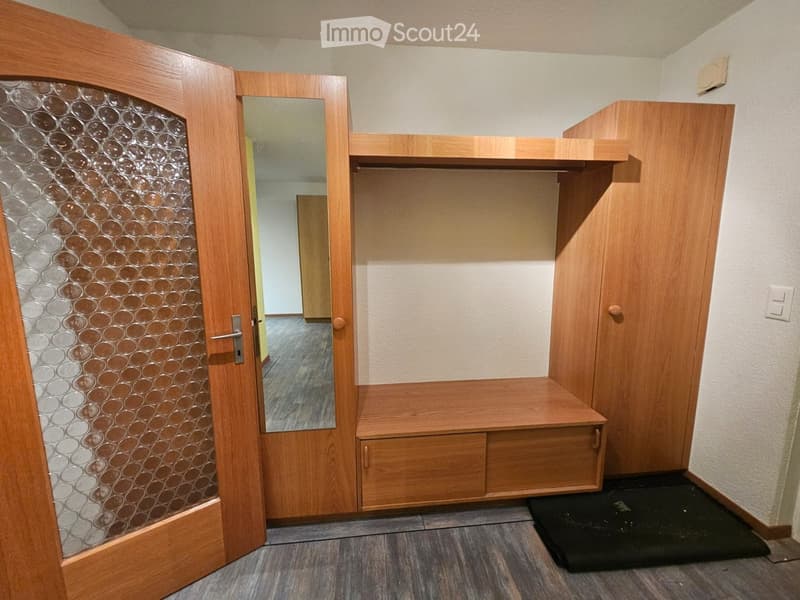 A modern hallway with wooden built-in storage, a mirrored door, and a small bench. The floor is tiled, and the walls are painted in a light color.