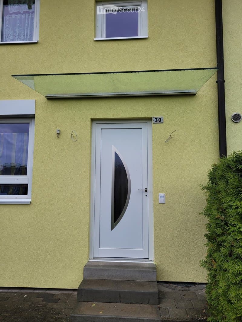Yellow building exterior with a raised entrance, white door with a curved glass panel, and a small canopy above.