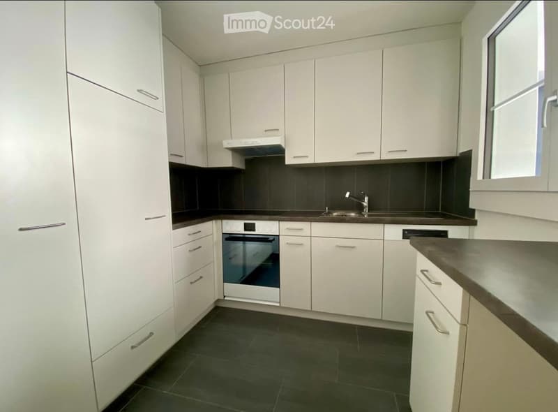Modern kitchen with white cabinets, dark countertops, and stainless steel appliances including an oven and sink.