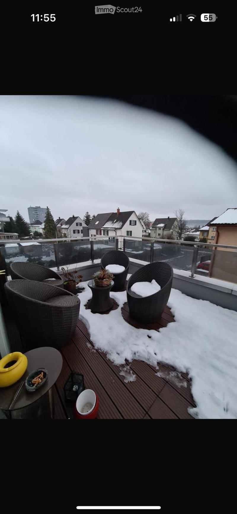 Balcony with wooden decking, snow patches, and a view of surrounding houses and trees.