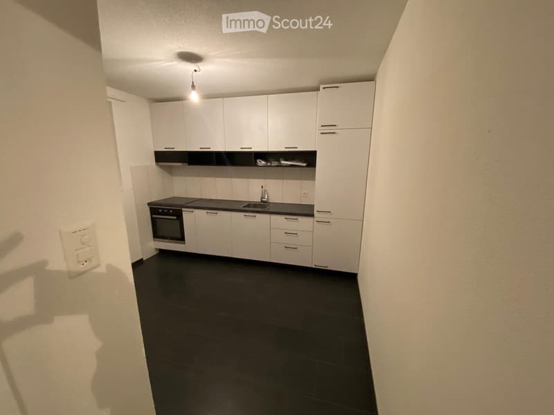 Modern kitchen with white cabinets, black countertops, and a dark tiled floor. Features an oven, sink, and faucet.