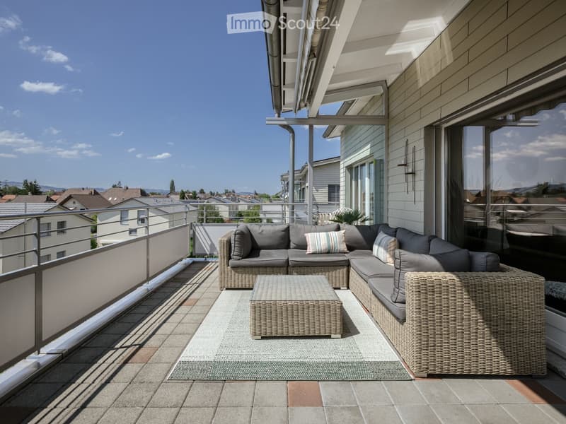 Balcony with modern wicker furniture, including a sectional sofa, coffee table, and armchair, overlooking a residential area.