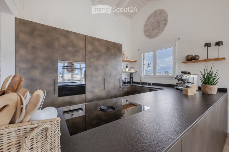 Modern kitchen with stainless steel cabinets, dark countertop, built-in appliances, and a view of the sea through large windows.