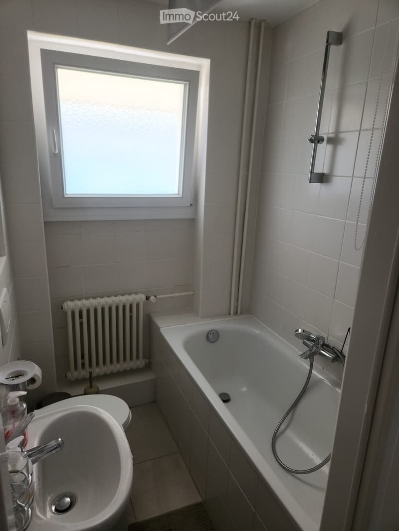 Bathroom with a bathtub, sink, toilet, radiator, and a window providing natural light.