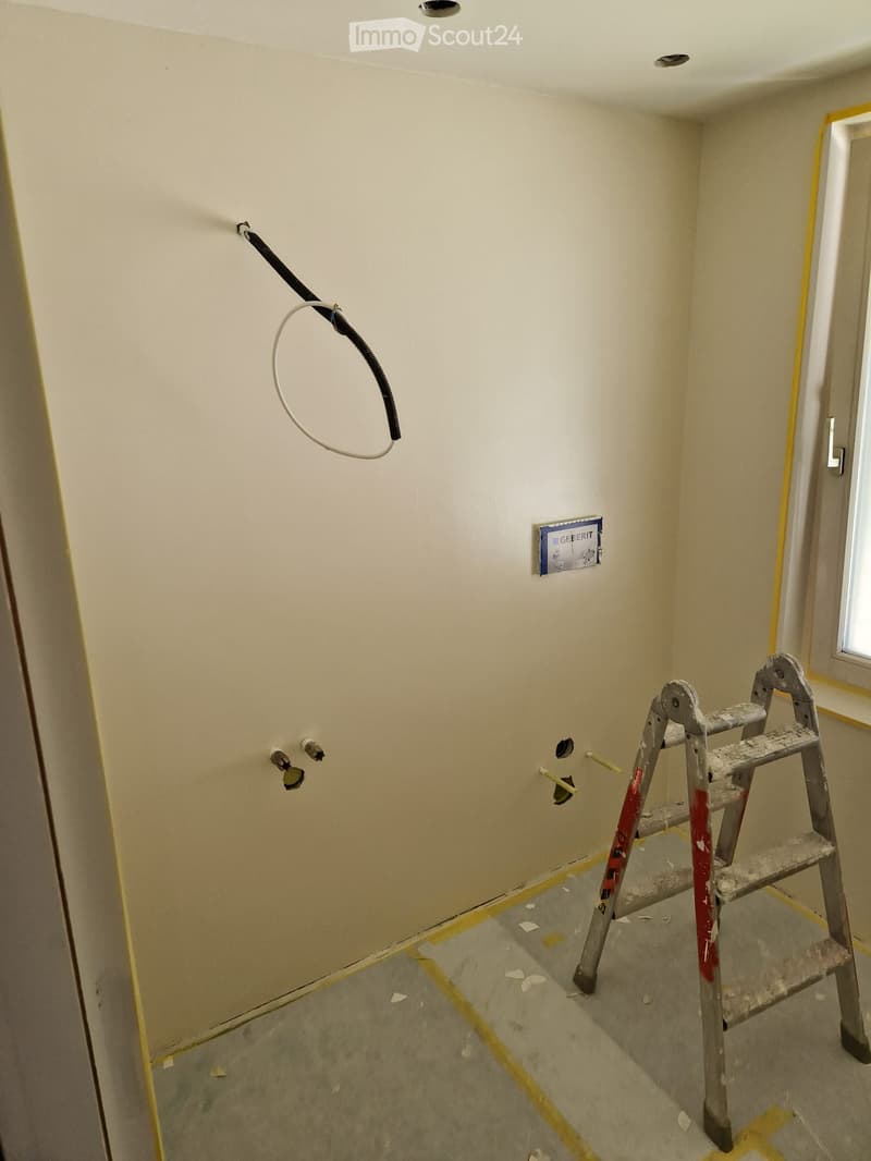 Empty room with bare walls and a concrete floor, featuring a ladder and some construction materials.