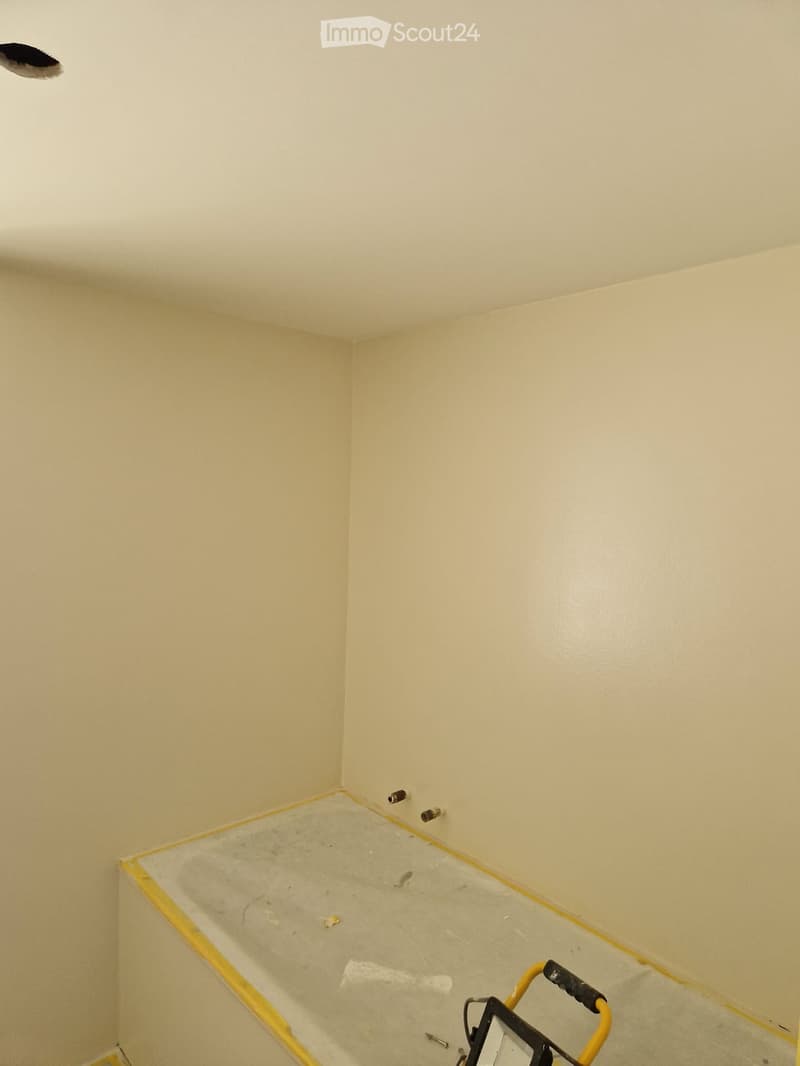 Empty room with light-colored walls and a concrete floor, showing construction materials and tools.