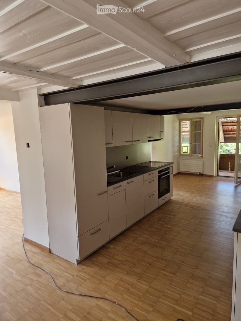 Modern kitchen with light-colored cabinets, a central island, and wooden flooring. Features include a sink, oven, and a window with a view of the outdoors.