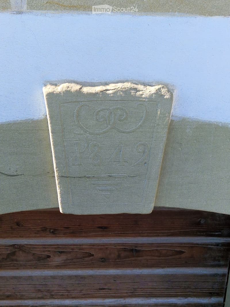 A close-up of a concrete block with an embossed logo and text, placed on a wooden surface against a white wall.