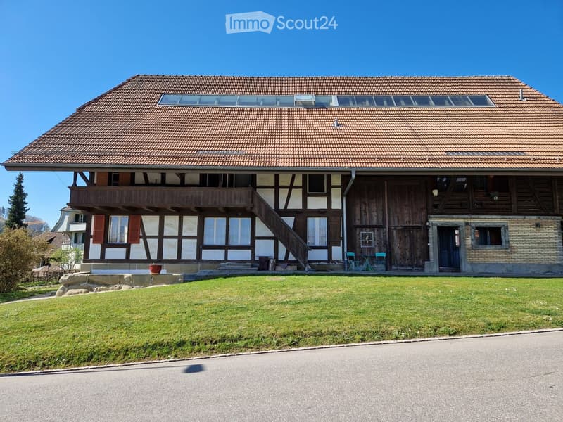 Two-story house with a tiled roof, wooden balcony, and a well-maintained lawn in front.