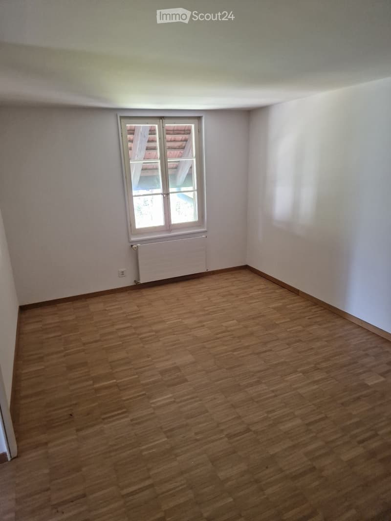 Empty room with wooden flooring, white walls, and a single window with a radiator below it.