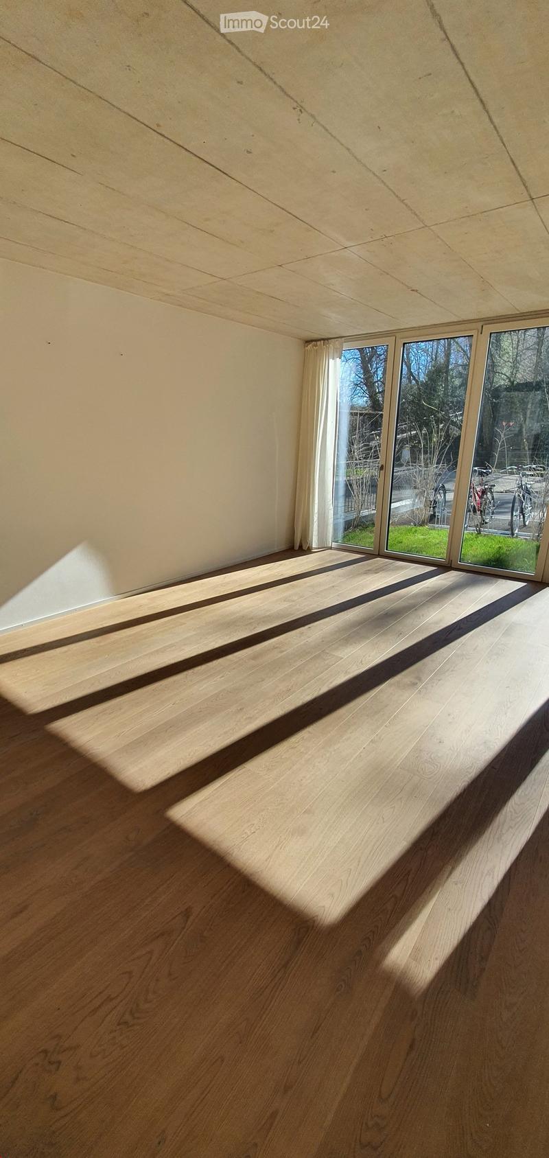 Empty room with wooden flooring and large windows, allowing natural light to fill the space.