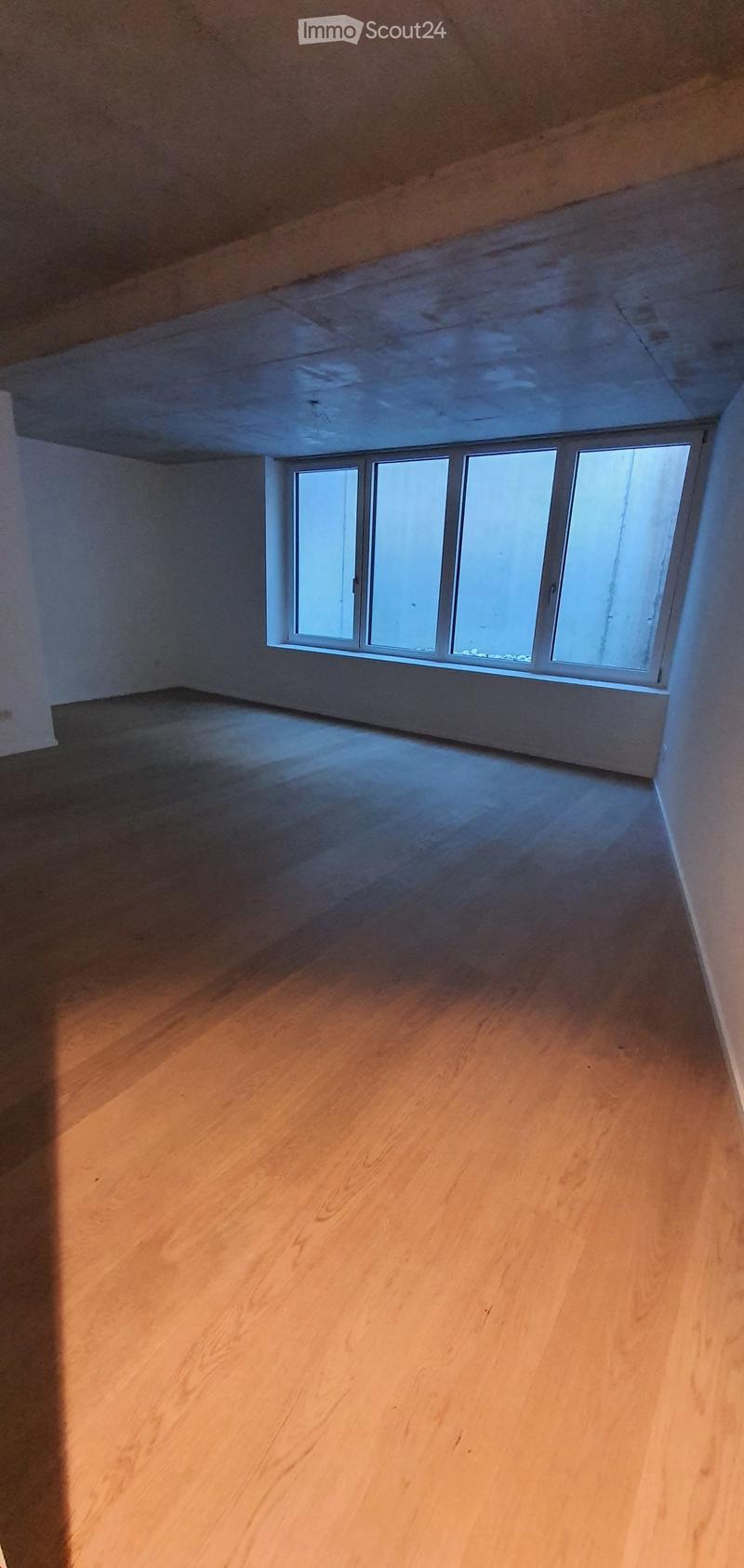 Empty room with wooden flooring and a single window letting in natural light. The walls are plain and there are no furnishings or decorations visible.