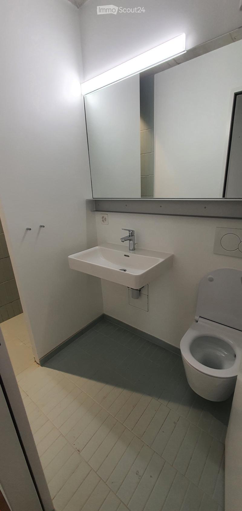 Modern bathroom with a white sink, chrome faucet, toilet, mirrored cabinet, and tiled floor.