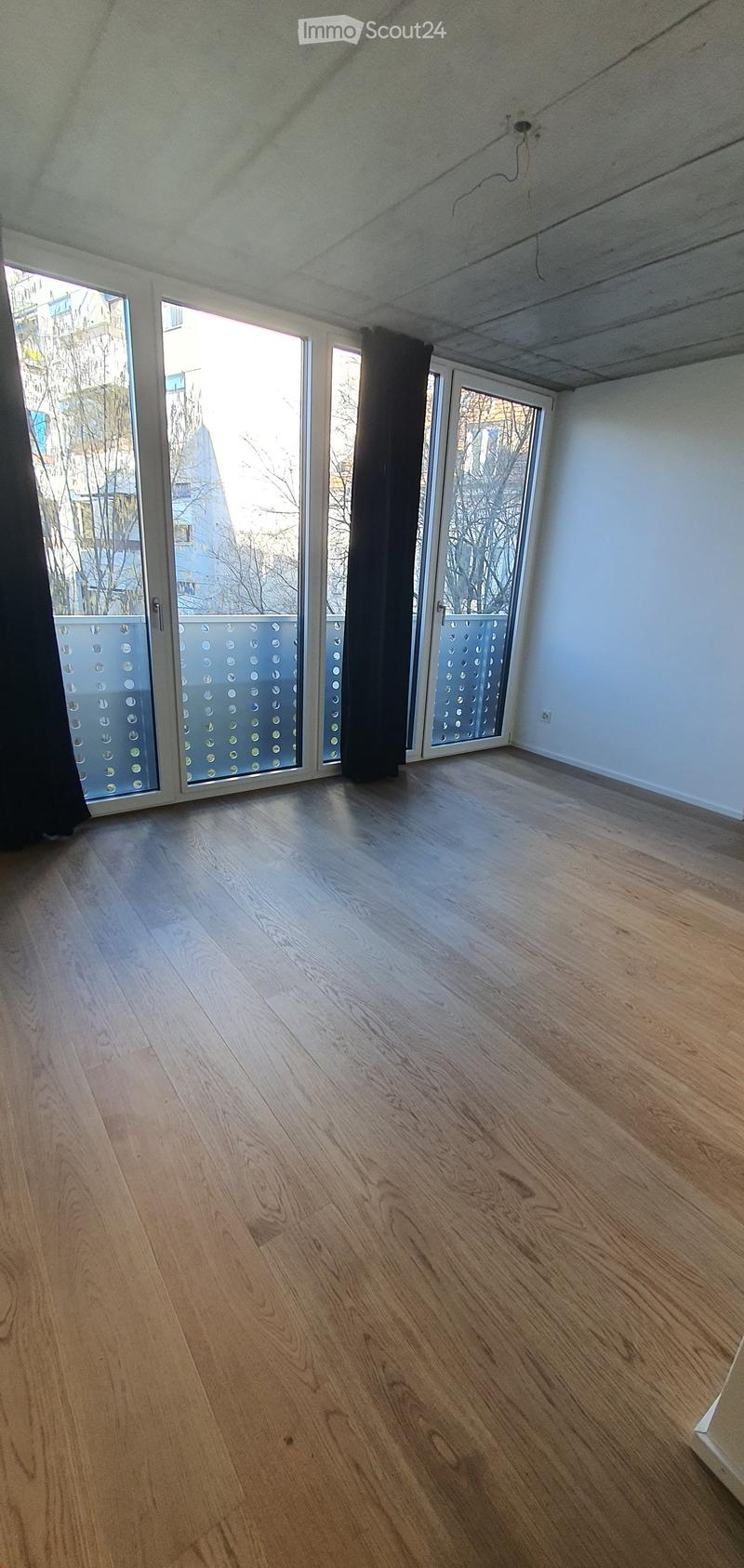 Empty room with light wooden flooring, large windows with frosted glass panels, and white walls.