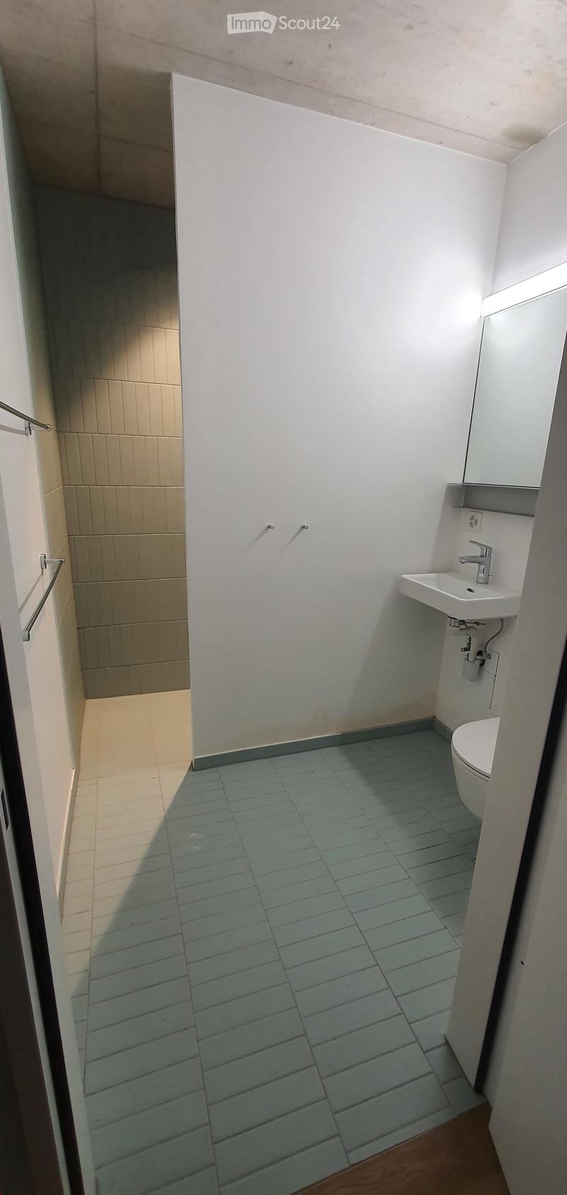 Modern bathroom with white walls, light blue tiled floor, a toilet, a sink with a modern faucet, and a small shelf above the sink.