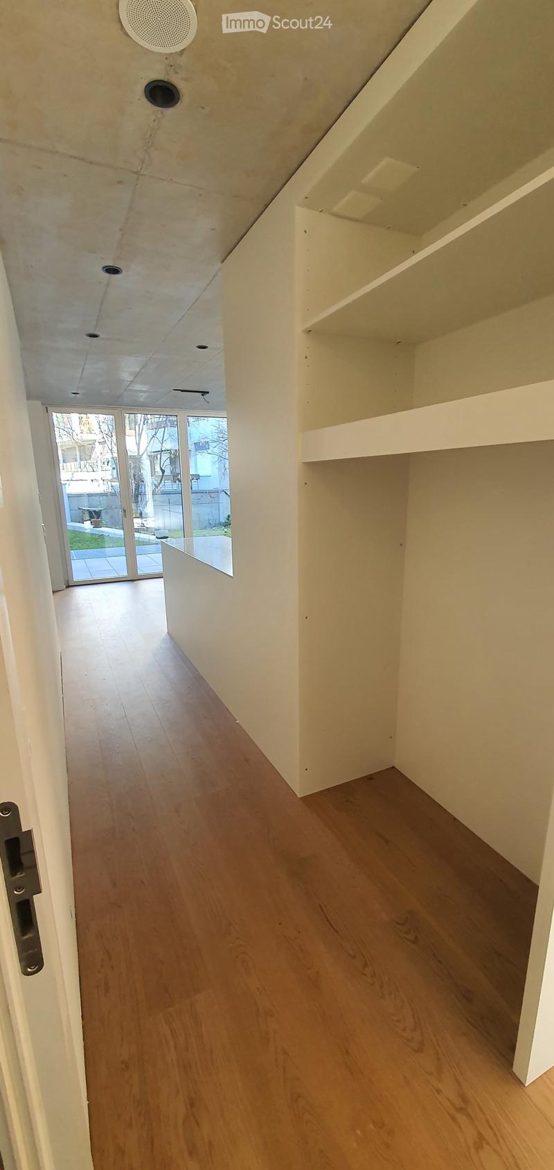 Empty hallway with light wooden flooring, white walls, and a glass door leading to an outdoor area.