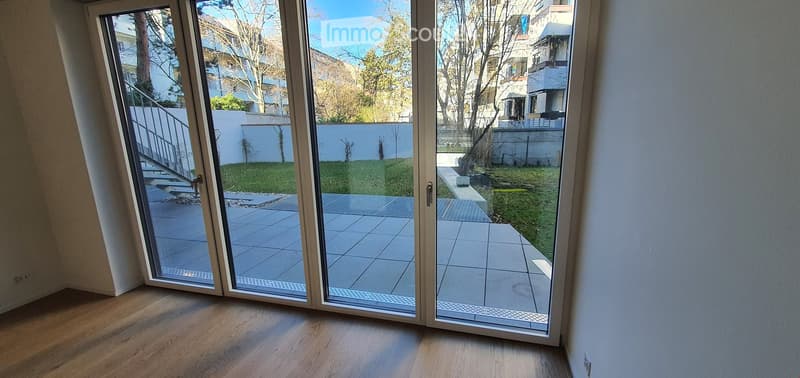 Empty room with wooden flooring and large sliding glass doors leading to a tiled patio and grassy garden area.