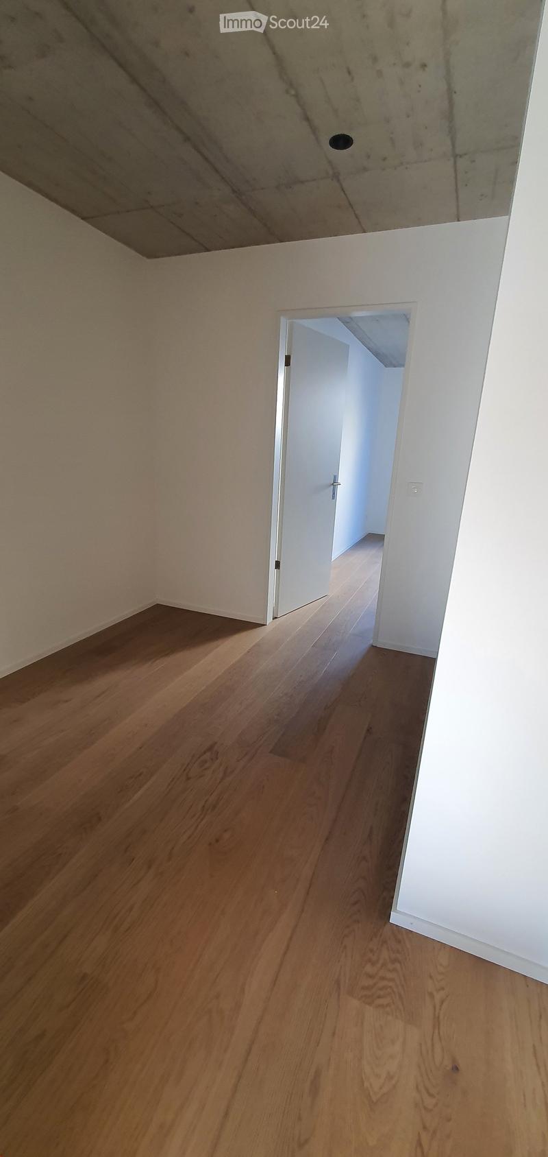 Empty room with wooden flooring and white walls, featuring a doorway leading to another space.