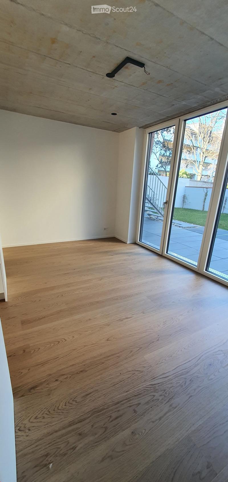 Empty room with light wooden flooring, white walls, and a large sliding glass door leading to an outdoor area.