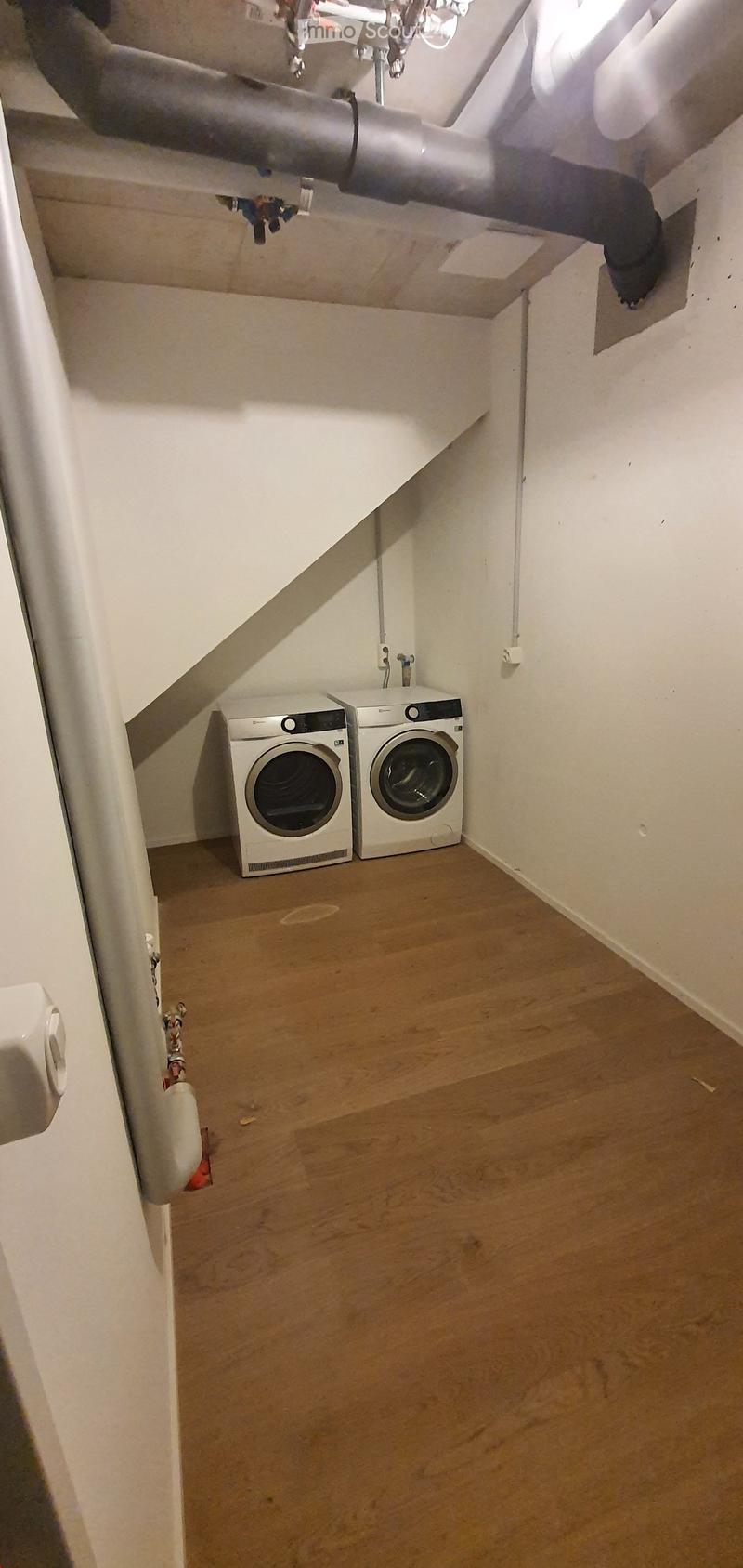 Small room with wooden flooring, white walls, and two stacked washing machines and dryers.