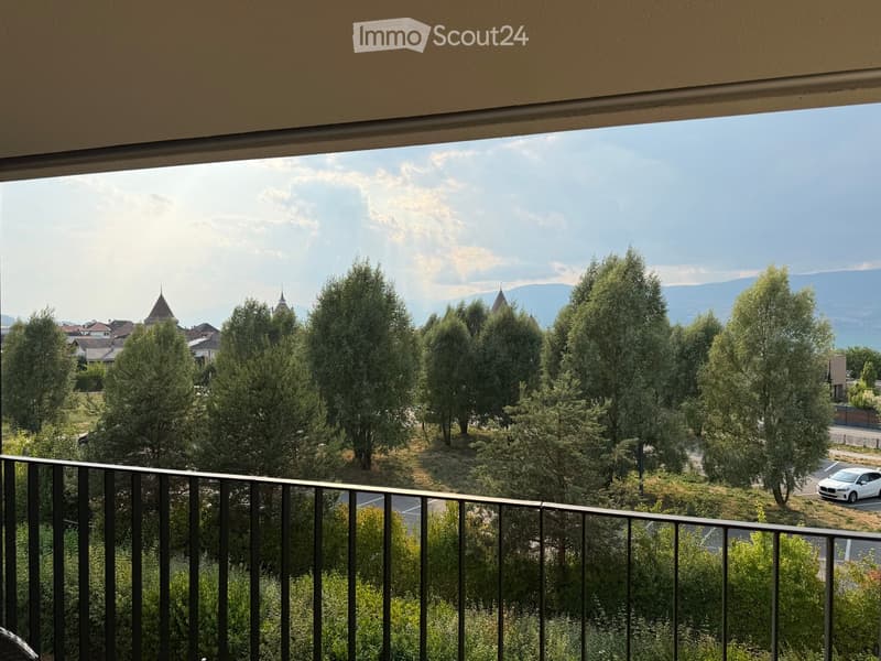 Balcony with metal railing overlooking a scenic view of trees, a small town with spires, and distant mountains.