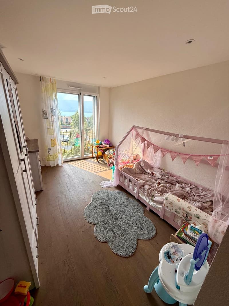 Child's bedroom with a bed, a small table, a chair, toys, a rug, and a view of the sea through large windows.