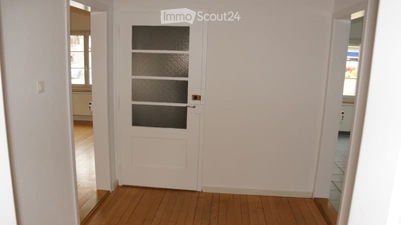 Empty hallway with wooden flooring, white walls, and a white door with frosted glass panels.