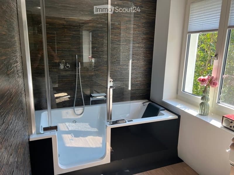 Modern bathroom with a large bathtub, glass-enclosed shower, and a vase of pink flowers on the windowsill.