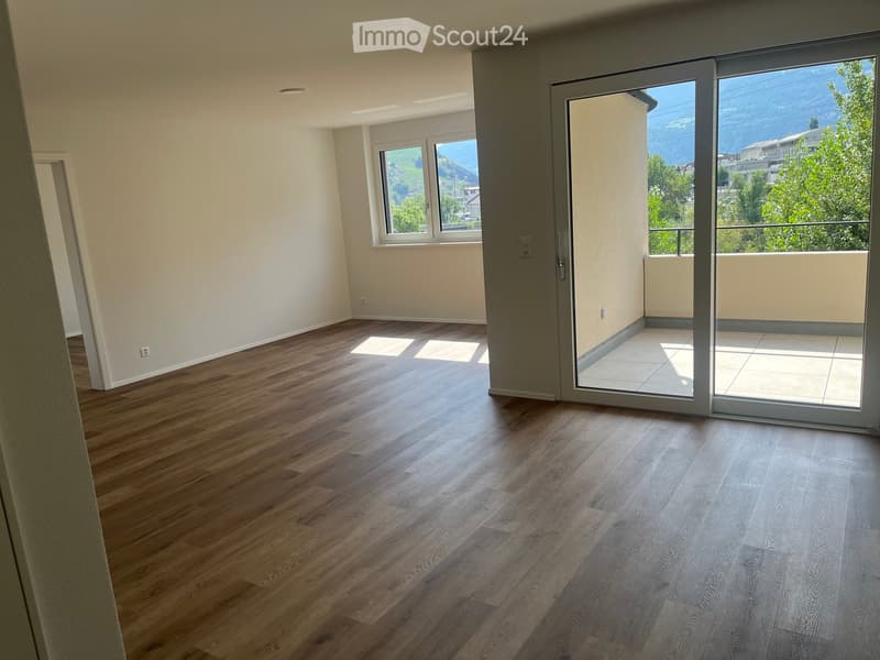 Empty room with wooden flooring, large windows, and a sliding glass door leading to a balcony with a scenic view.