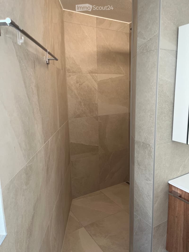 Modern hallway with beige marble tiles, a stainless steel handrail, and a built-in wooden cabinet with a white countertop.