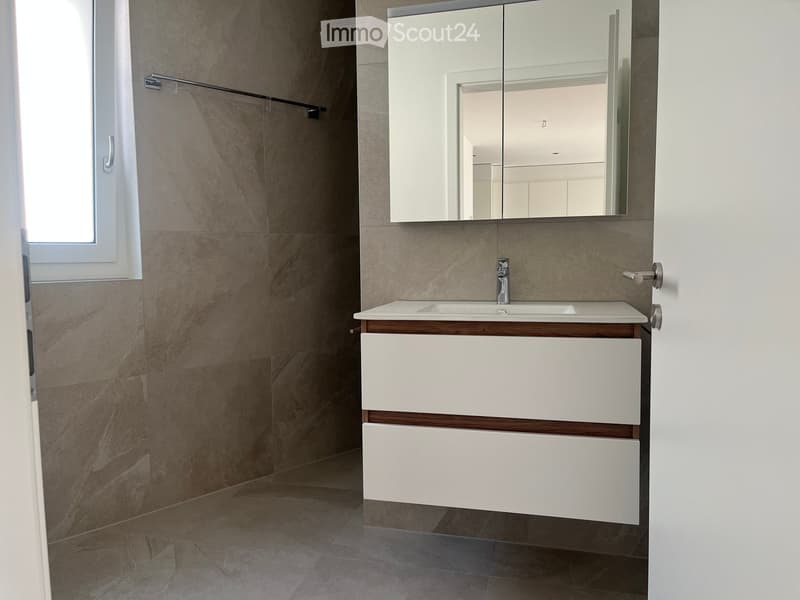 Modern bathroom with a white vanity, marble tiles, and a large mirror above the sink.