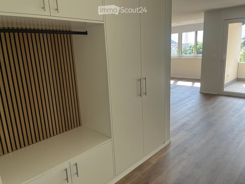 Empty room with light-colored wooden flooring, white built-in closet with multiple sections and a rod for hanging clothes, and a large window with a view of the outside.